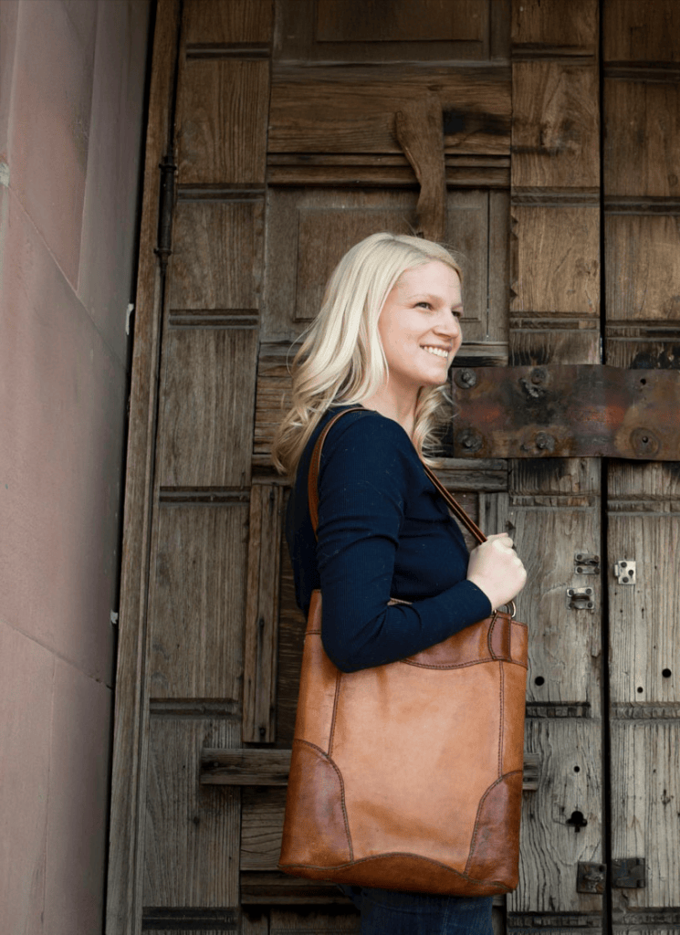 Jenna Westbrook with a leather tote bag in front of a weathered wooden door